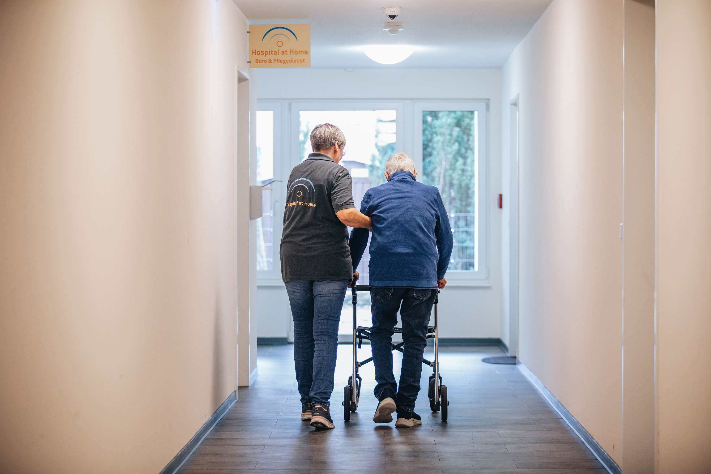 Alter Mann mit Gehwagen und Pflegerin an der Seite